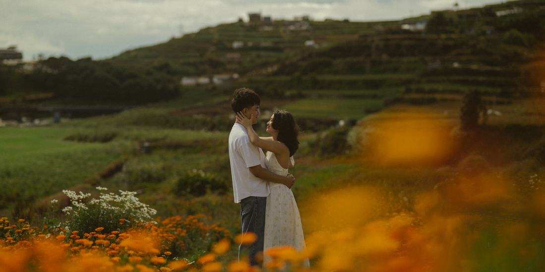 Bryan and Irey holding each other on a terraced hillside, marigolds blurred in the foreground.