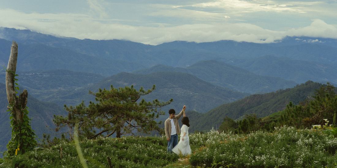 Bryan lifting Irey's hand as they turn together on a ridge above the clouds.